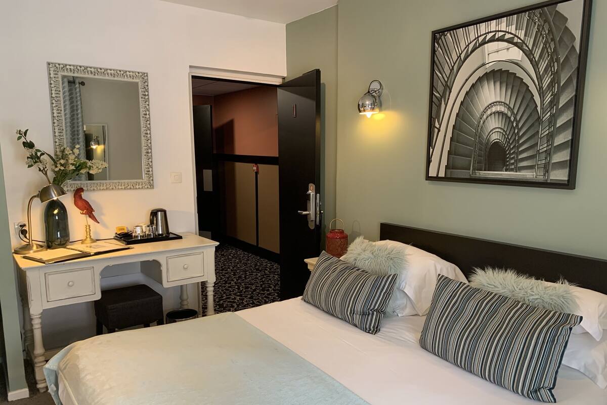 Ein Hotelzimmer mit Bett, Schreibtisch, Spiegel, einem Gemälde und einer Treppe.