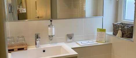 Een badkamer met een wit wastafel, spiegel en toilet. Boven het wastafel hangt een handdoekrek en er is een raam met uitzicht op buiten.