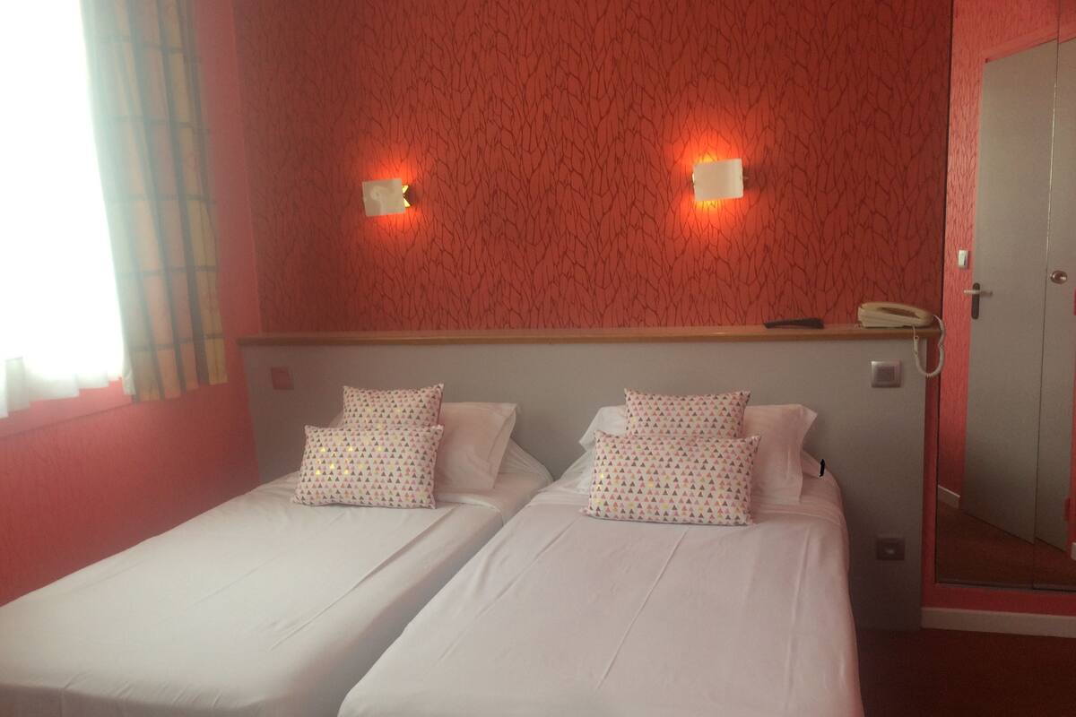 Une chambre d’hôtel avec deux lits simples, un mur décoré d’un motif rouge et un téléphone sur la table de chevet.