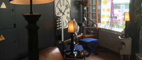 A living room with a brown leather sofa, a large wall clock, and a window with a view of the outside.