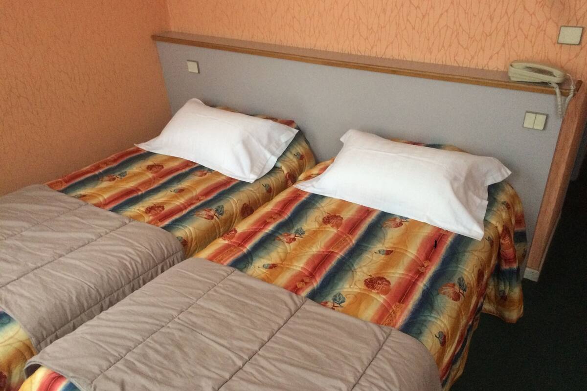 Un lit double avec une literie à motifs floraux et deux oreillers, un téléphone sur la table de chevet et une prise électrique au mur.