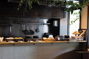 A kitchen counter with various food items and utensils, a hanging pot rack, and a window with natural light. - Madrigal hotel (Paris)