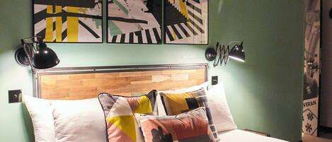 A hotel room with a bed, pillows, a blanket, and a wall with abstract art.
