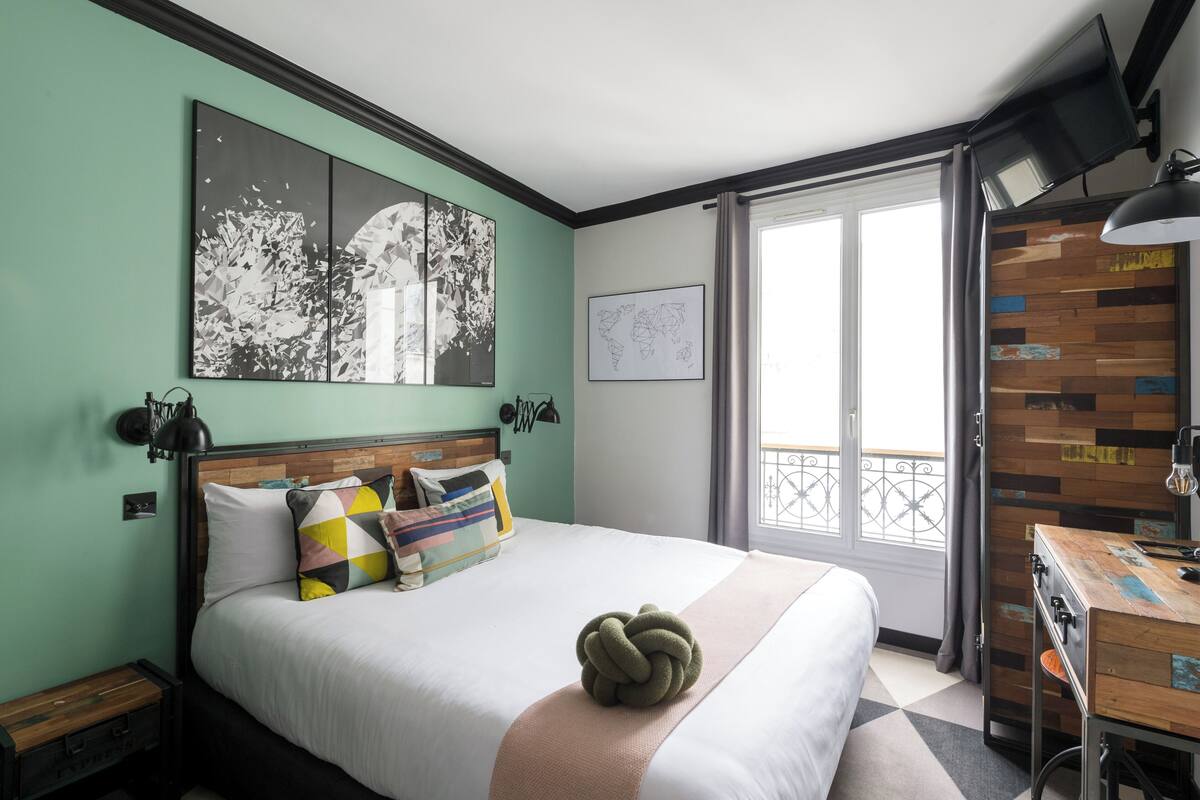A neatly arranged bedroom with a bed, pillows, a wall-mounted TV, and a wooden desk.