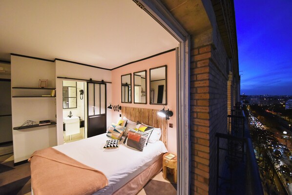 Une chambre moderne avec un grand lit, des tables de chevet, un miroir et une vue sur la ville la nuit.