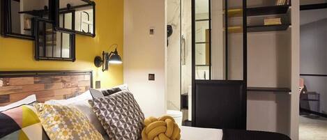 Ein Hotelzimmer mit einem Bett, einem Kopfteil, einem Spiegel, einer Lampe, einem Kleiderschrank und einer Schiebetür zu einem Badezimmer.