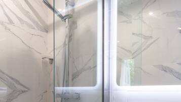 A modern bathroom with a glass-enclosed shower, a white sink, and a marble-patterned wall.