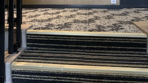 Un pasillo de hotel con una escalera alfombrada que conduce a una puerta marcada con el número 303. Señales direccionales indican los números de habitación 304-307 a la izquierda y 301-303 a la derecha.