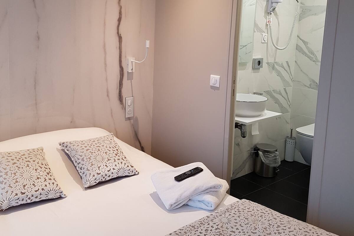 Habitación de hotel moderna con pared de mármol, cama con almohadones estampados, control remoto y baño visible a través de una puerta abierta.