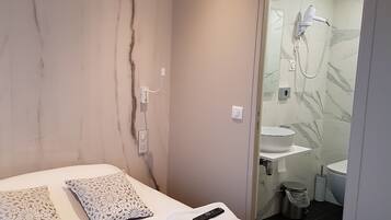 Habitación de hotel moderna con pared de mármol, cama con almohadones estampados, control remoto y baño visible a través de una puerta abierta.