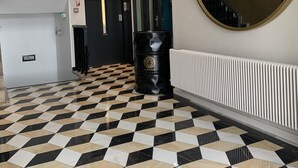 Un pasillo con piso a cuadros, un espejo grande y un radiador.