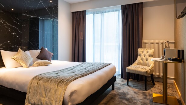 Habitación de hotel con una cama grande, una silla, una mesita y una ventana con cortinas.