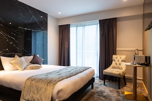A hotel room with a large bed, a chair, a small table, and a window with curtains. - Hôtel d’Angleterre Rouen Centre (Rouen)