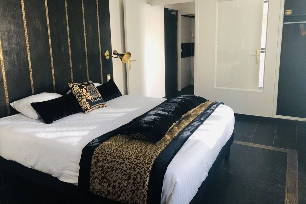Una habitación de hotel con una cama grande, un cabecero con estampado dorado y negro, y una puerta blanca.