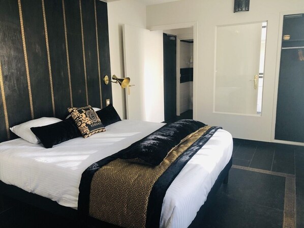 Una habitación de hotel con una cama grande, un cabecero con estampado dorado y negro, y una puerta blanca.