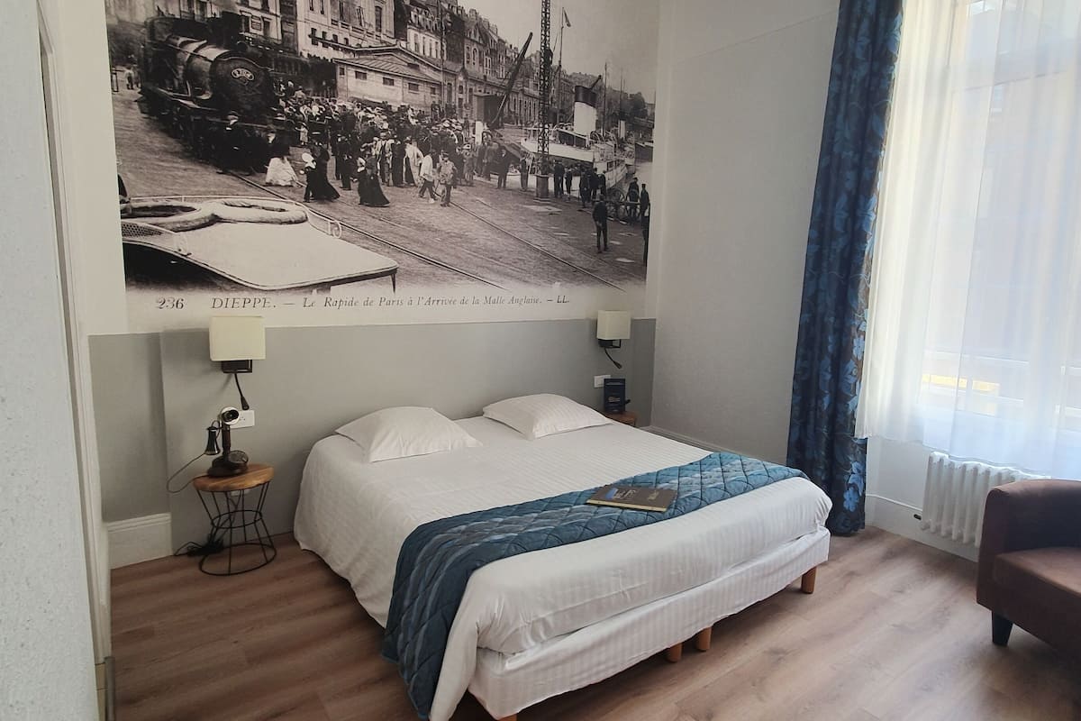 Un dormitorio con una cama grande, una silla, una lámpara y un cartel antiguo en la pared.
