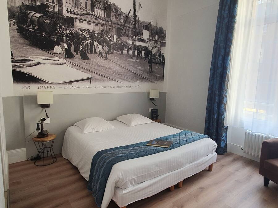 A bedroom with a large bed, a chair, a lamp, and a vintage poster on the wall.