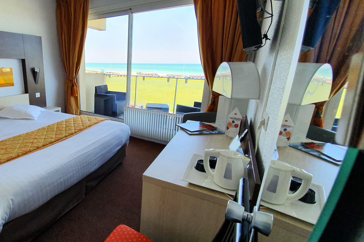 Habitación de hotel con cama, escritorio con cafetera y vista a la playa.