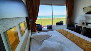 Habitación de hotel con cama, escritorio, silla, televisor y vista a la playa.