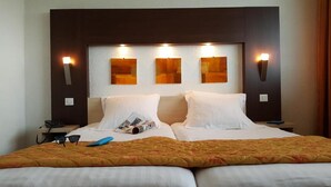 Una habitación de hotel con una cama grande, dos mesitas de noche y tres luces fijadas a la pared.