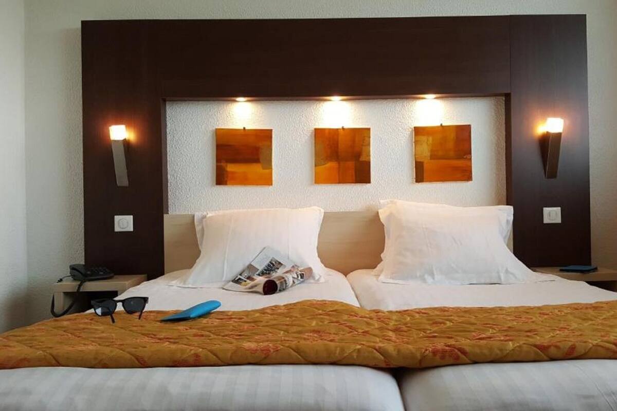 Una habitación de hotel con una cama grande, dos mesitas de noche y tres luces fijadas a la pared.