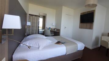 A hotel room with a bed, bedside lamps, a desk, a chair, a TV, and a window with curtains.