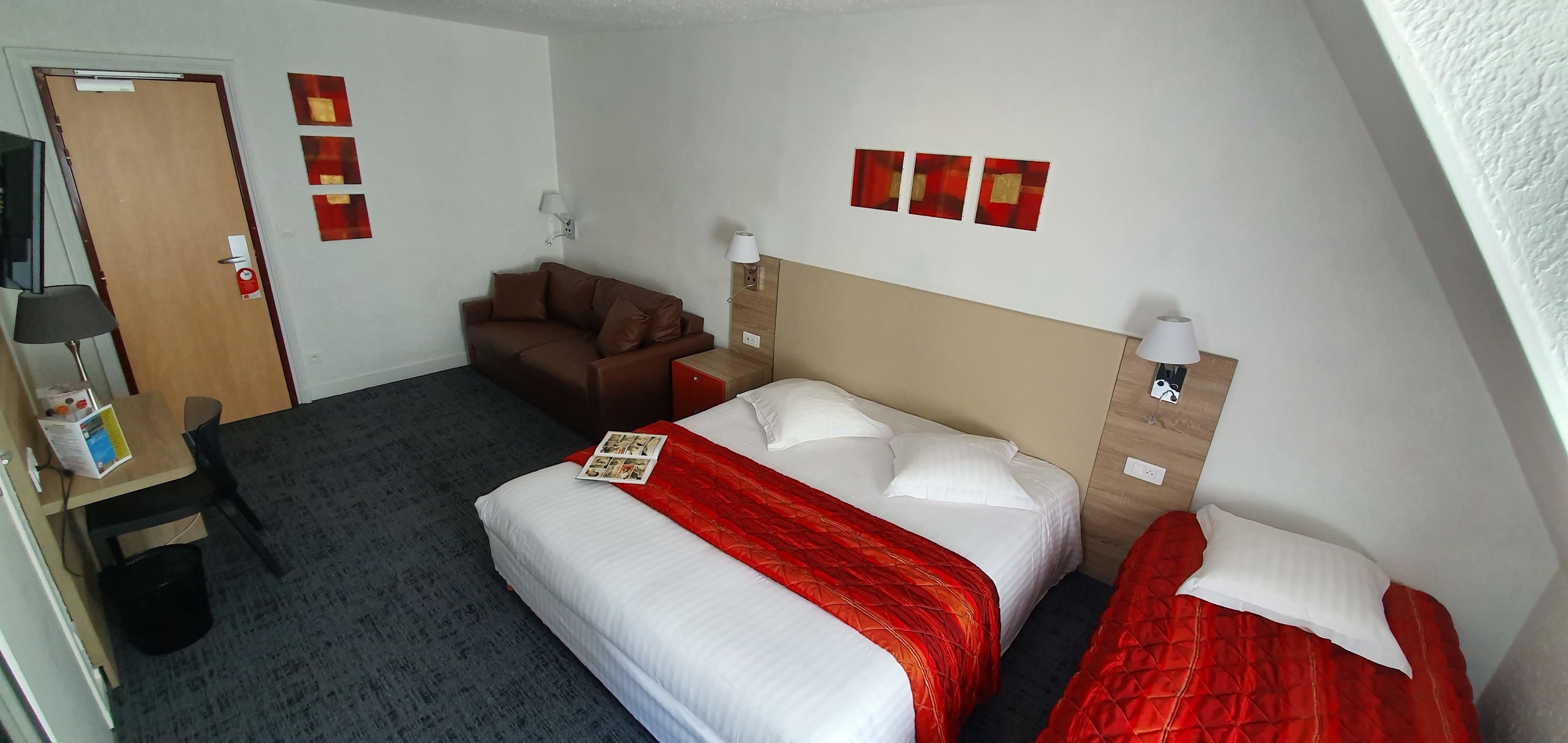 A hotel room with a bed, a sofa, a desk with a chair, and a TV.