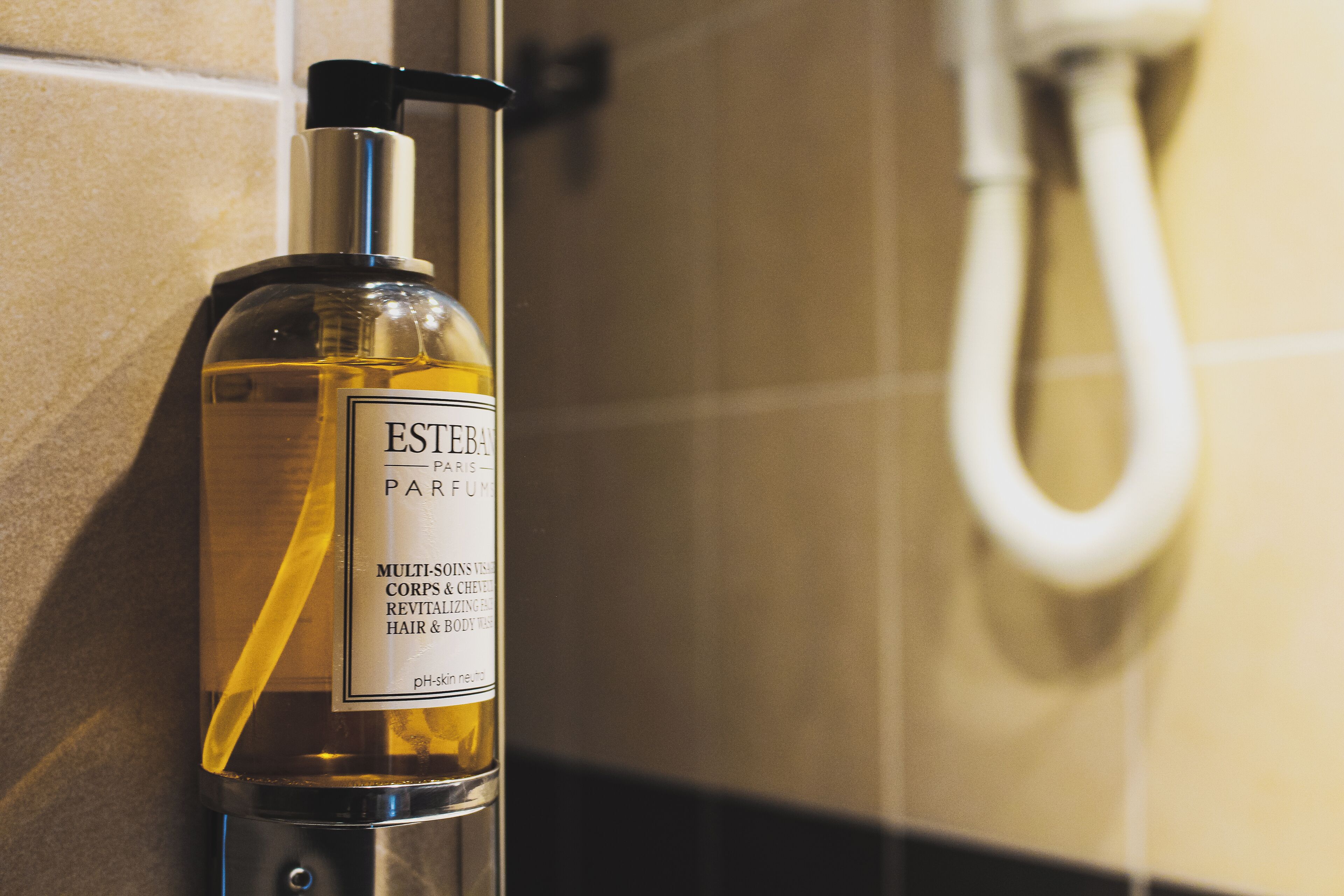 A bottle of Ester Paris Parfum with a pump dispenser, placed against a tiled wall.