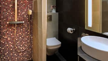 Un baño moderno con ducha de mosaicos, inodoro y un lavamanos grande con espejo.