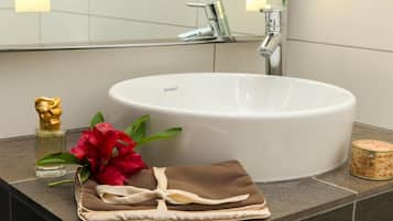 Un baño con un lavamanos blanco, una estatua dorada, una flor roja y una toalla marrón sobre el mostrador.