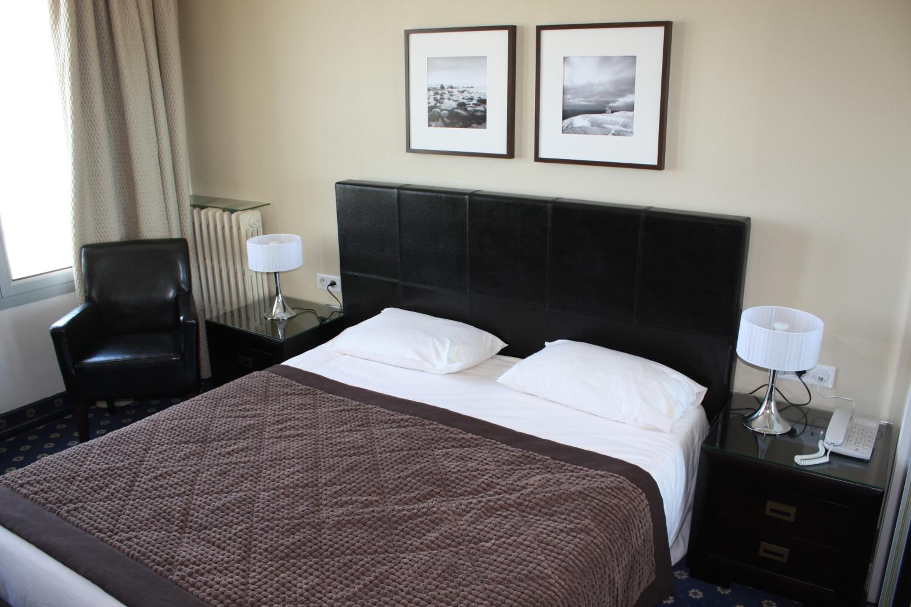Une chambre d’hôtel avec un grand lit, deux tables de chevet, une chaise et deux tableaux encadrés au mur.