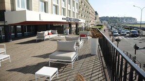 A hotel with outdoor seating, a paved terrace, and a view of the street and vehicles. - Hotel Aguado (Dieppe)