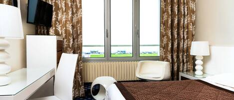 A hotel room with a bed, desk, chair, and a window with curtains.