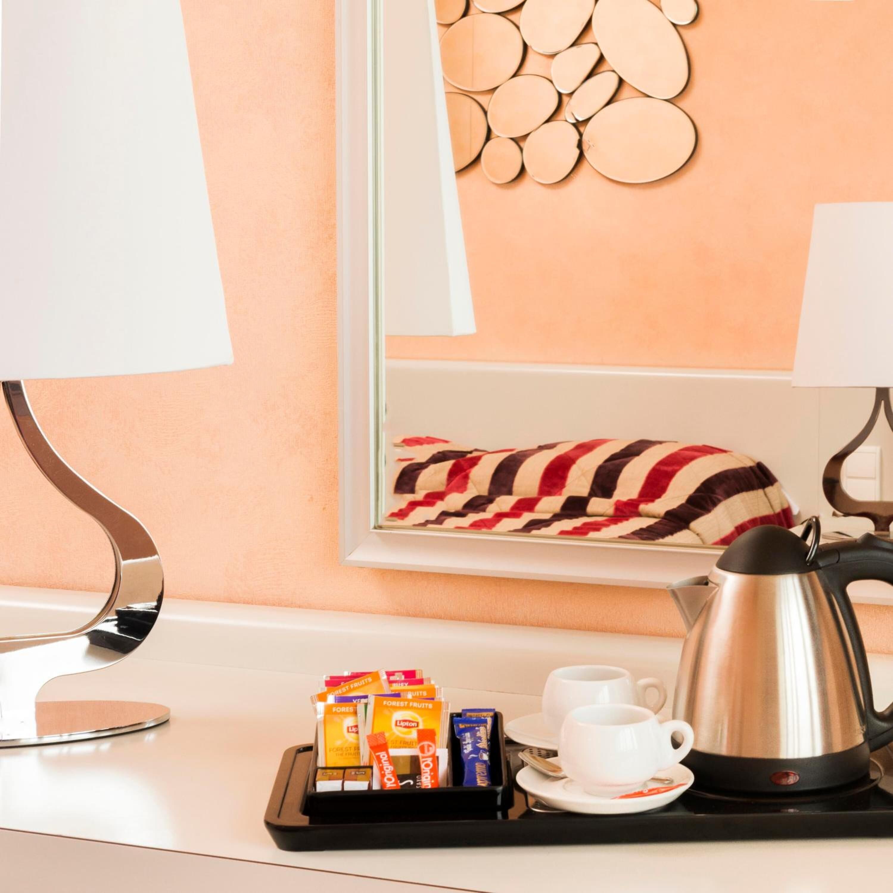 Een hotelkamer met een modern design, met een wit bureau, een schotel met snacks, een waterkoker en een ingelijst beeld aan de muur.