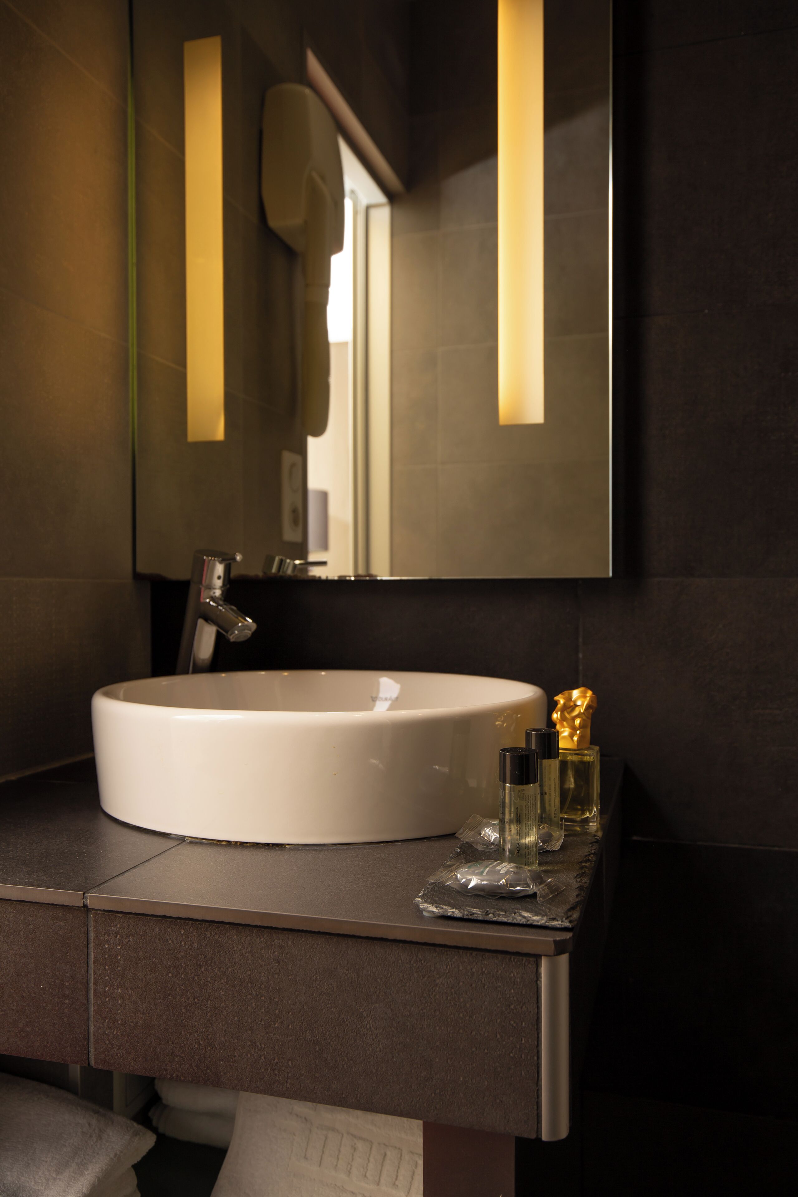 A modern bathroom with a large white sink, a mirror, and a dark countertop.