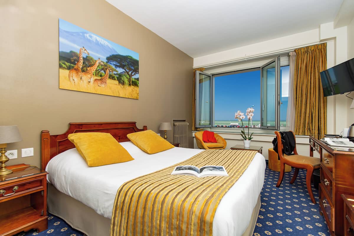 A hotel room with a bed, a desk, a chair, a TV, and a window with a view.