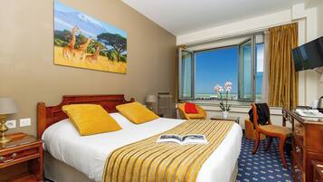 Habitación de hotel con cama, escritorio, silla, televisor y ventana con vistas.