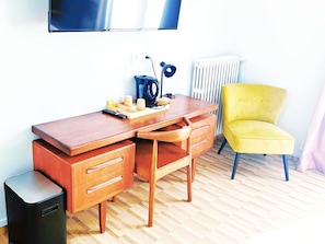 A wooden desk with drawers, a chair, a radiator, and a television mounted on the wall.