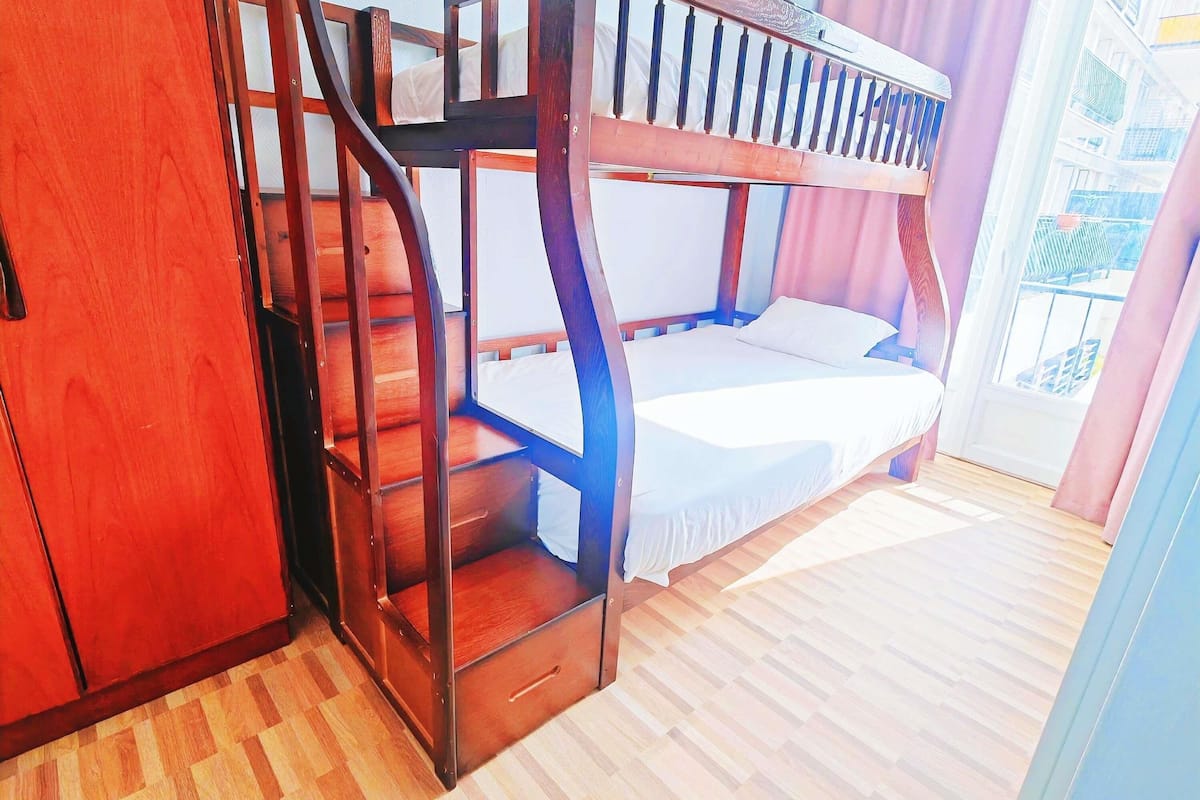 Dormitorio con literas, una escalera de madera y una ventana.