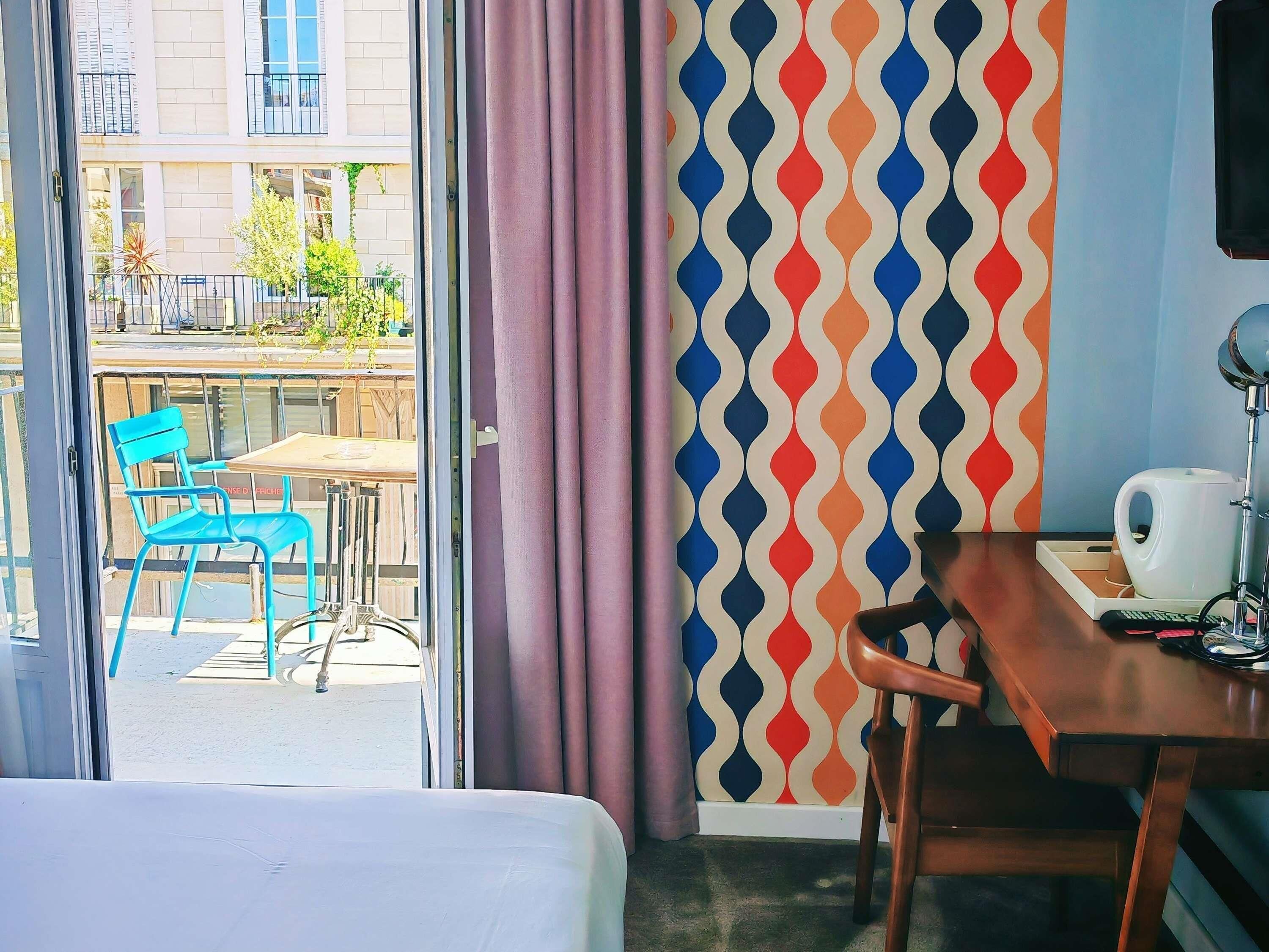 Habitación de hotel con cama, escritorio, silla, mesa, cafetera y vistas al exterior.