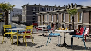 Una terraza con mesas y sillas para exterior, y vistas a un edificio con varias ventanas y balcones.
