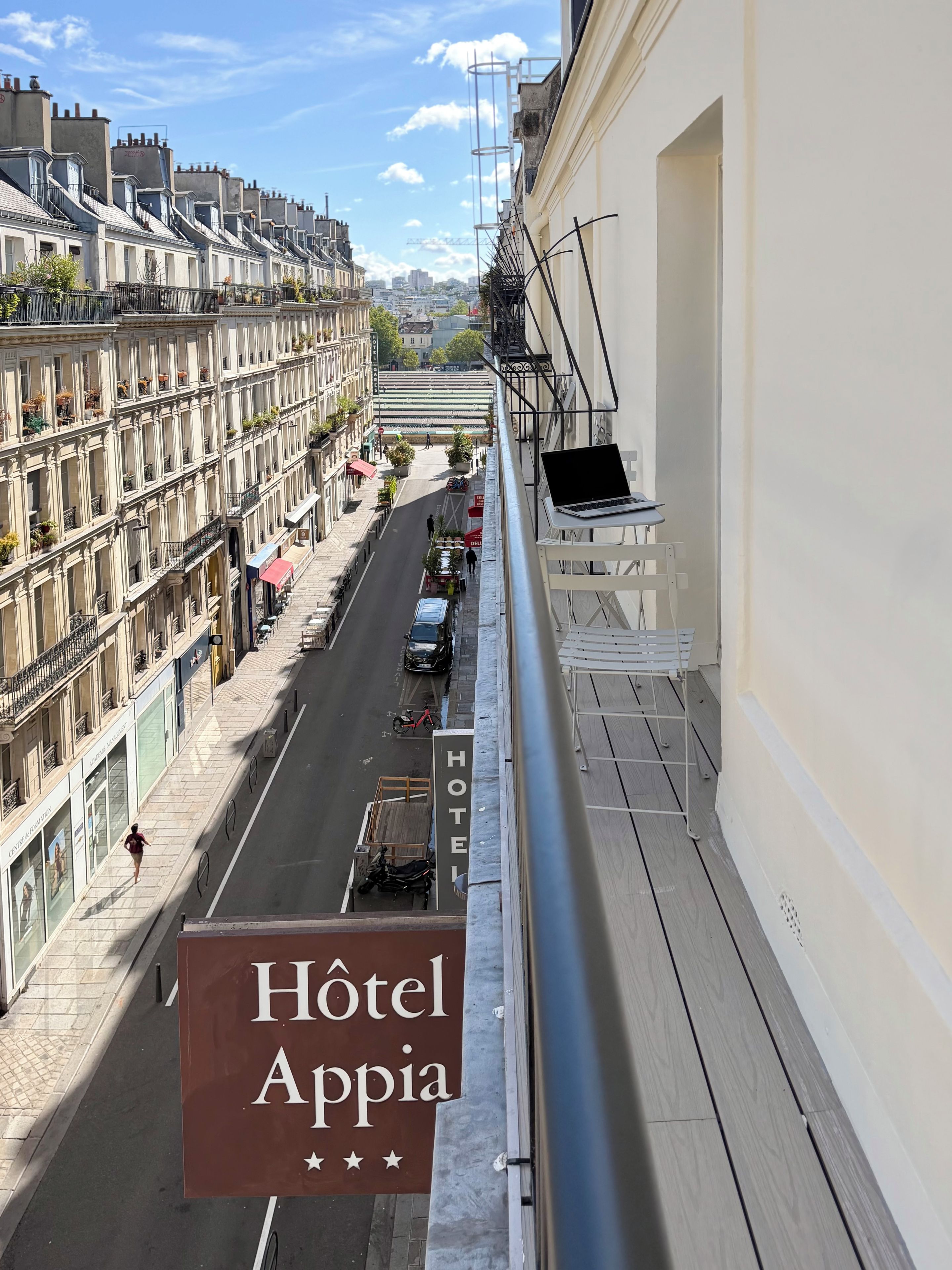 Señal de hotel con 'HOTEL Appia' y vista de una calle con edificios y coches aparcados.