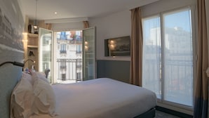 Una habitación de hotel con una cama grande, una puerta de vidrio que da a un balcón y vistas de la ciudad.