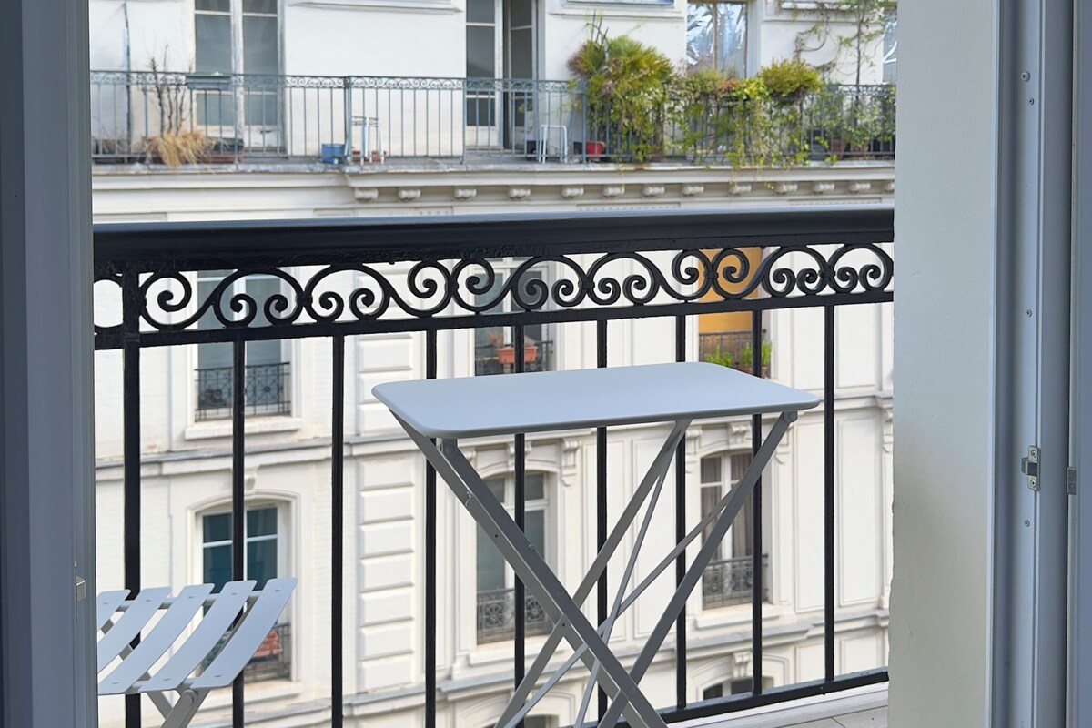 A balcony with a table and chairs, overlooking a row of buildings with classic architecture.