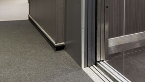 A modern elevator with a metallic finish and a glass door, adjacent to a hallway with a carpeted floor and a door at the end. - Appia La Fayette (Paris)