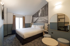 A hotel room with a large bed, a round table, a mirror, and a painting of a railway track. - Appia La Fayette (Paris)