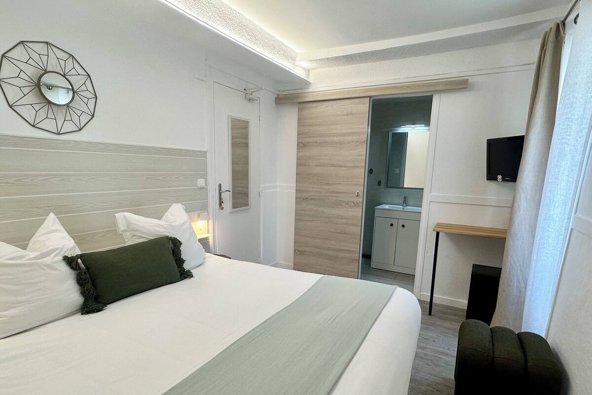 A hotel room with a bed, a desk, a TV, and a bathroom visible through an open door.