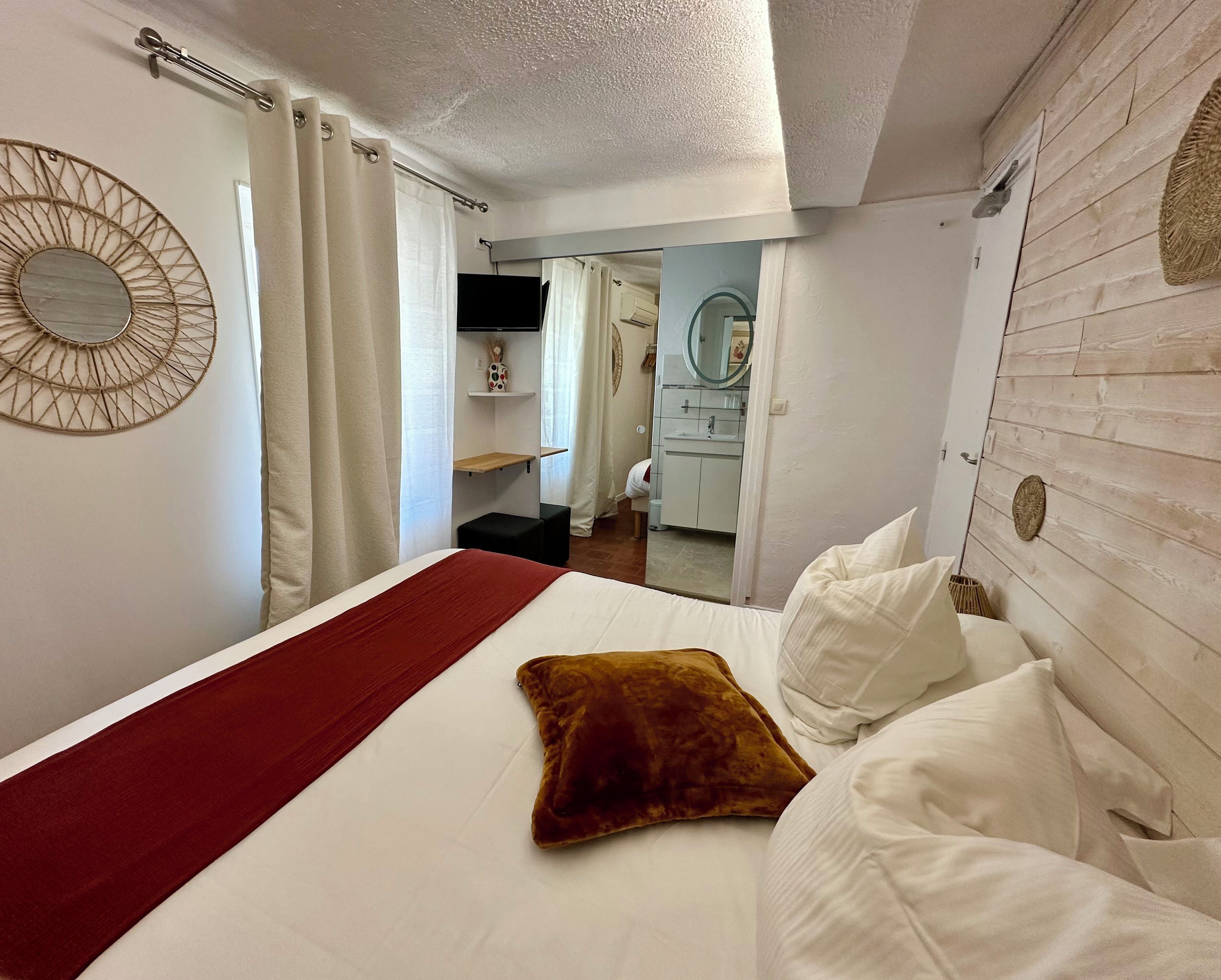 Une chambre à coucher avec un lit, un plaid rouge, un oreiller marron, un miroir et un mur en bois.