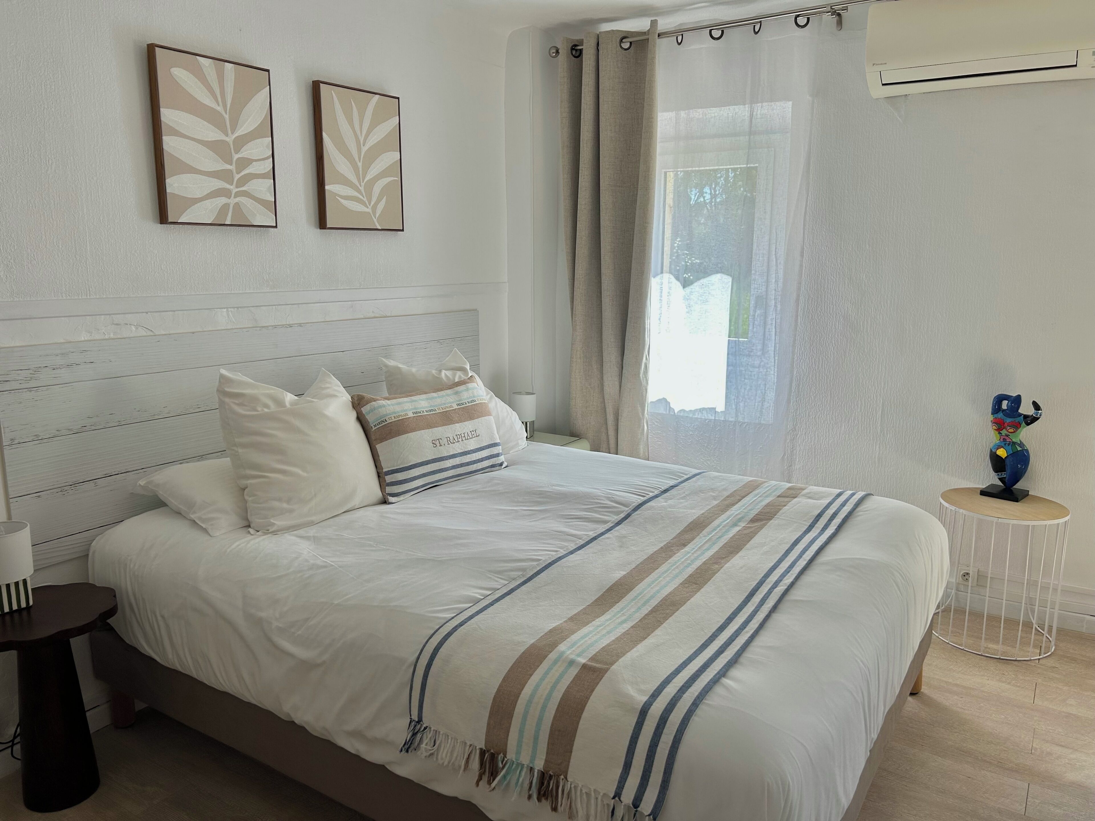 A neatly made bed with a striped blanket, a bedside table with a lamp, and two wall-mounted art pieces.