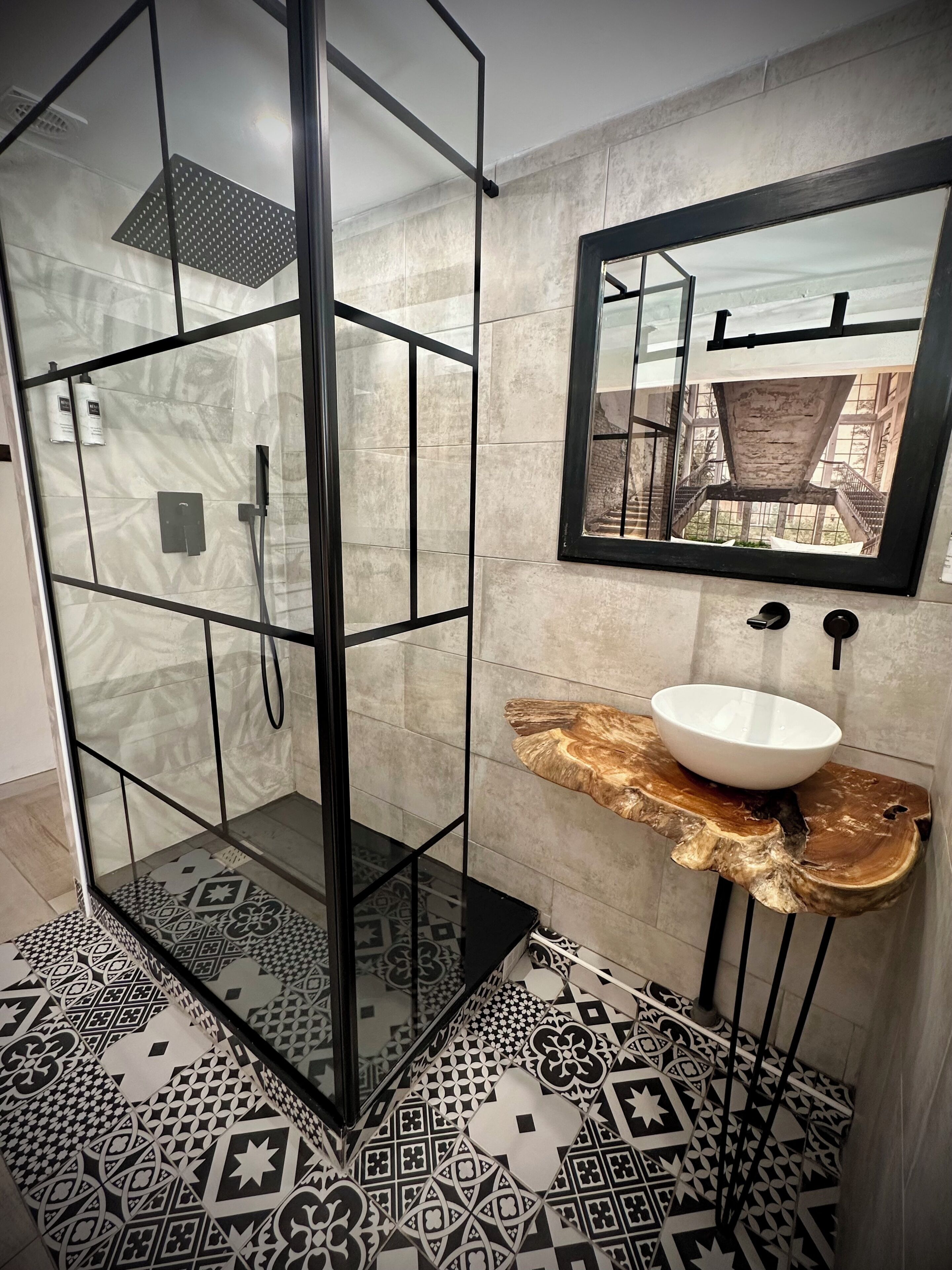 A modern bathroom with a glass-enclosed shower, a marble-tiled floor, and a unique wooden basin.